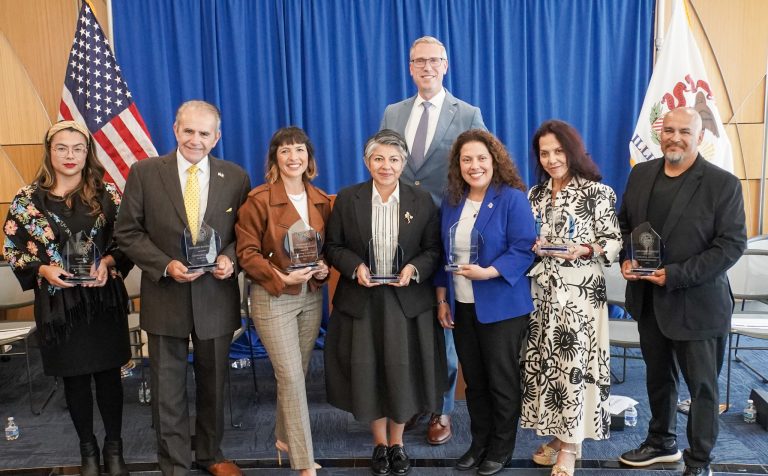 Treasurer Frerichs posing against a blue curtain and the U.S. flag with recipients of Hispanic Heritage Month awards in 2025