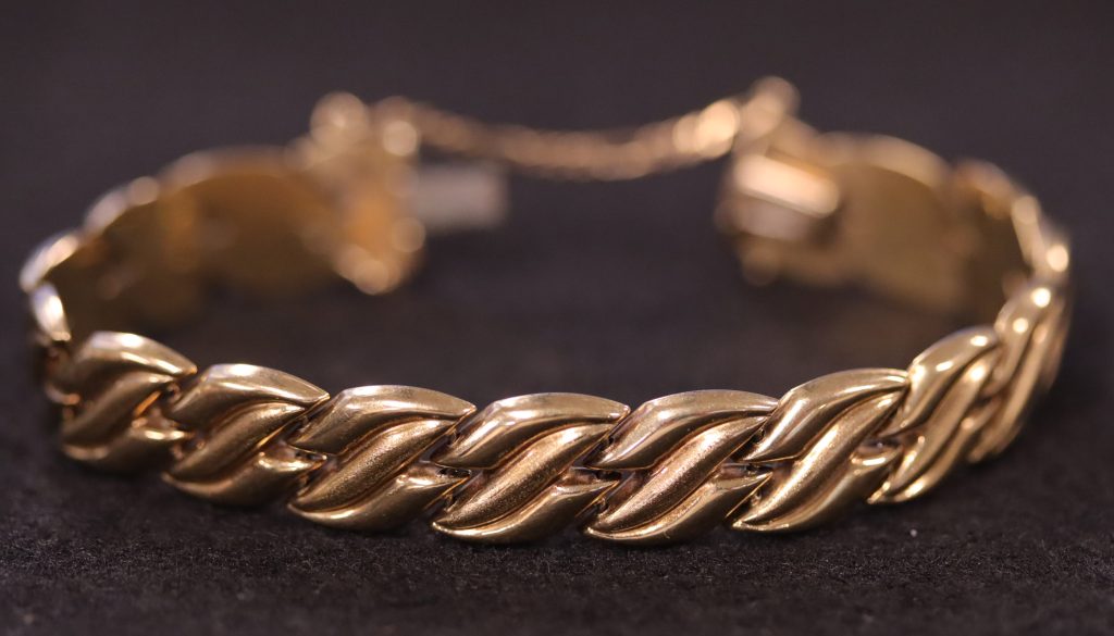 gold bracelet with a braid pattern sitting on black background