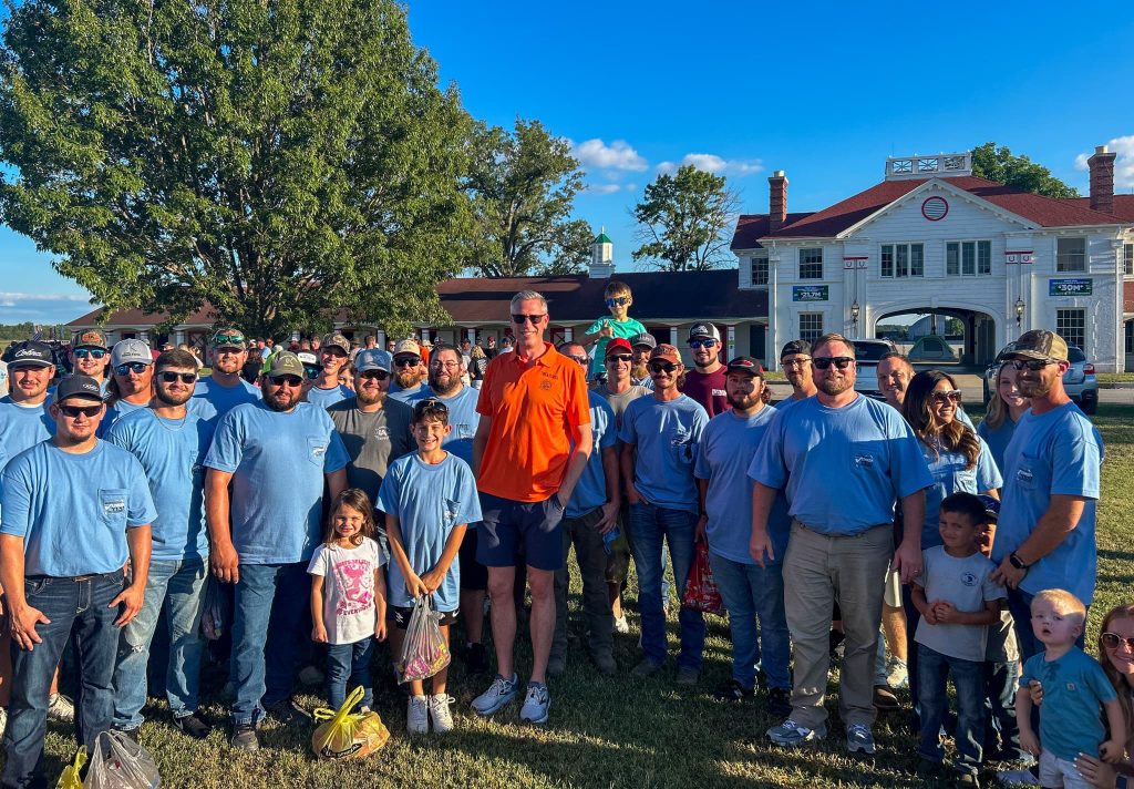 a man in an orange shirt stands in the middle of a crowd at a summer festival