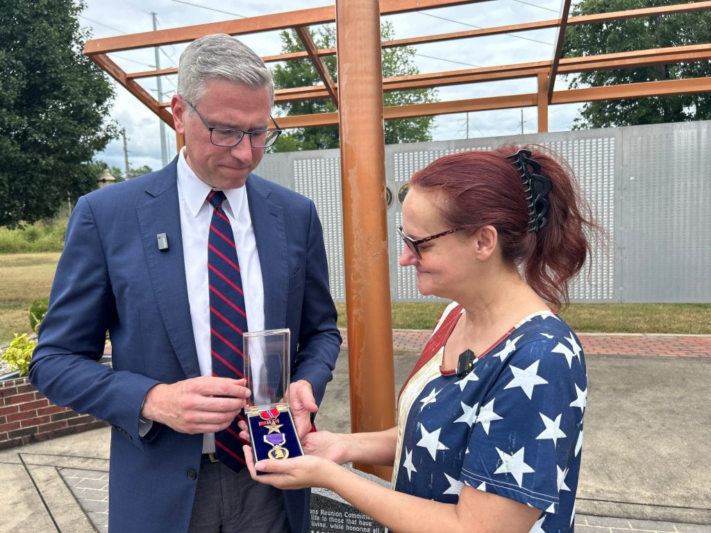 a man and a woman stand under an open air awning looking at a purple heart medal in a case