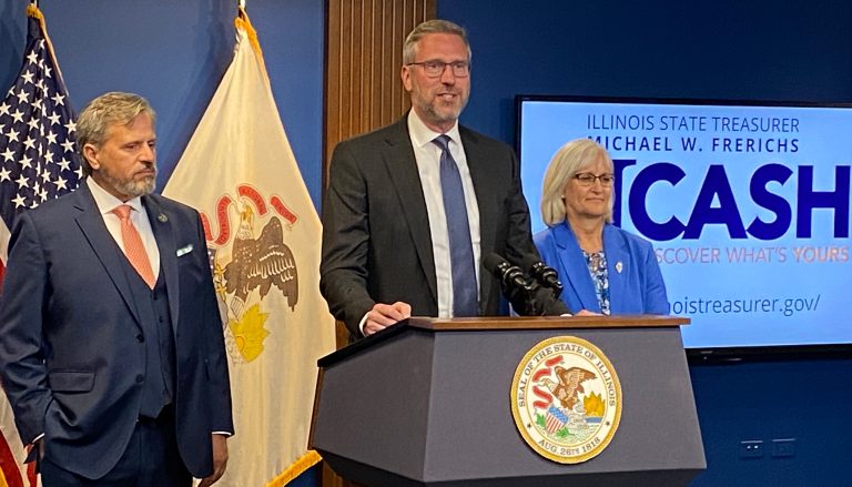 Treasurer Frerichs stands and speaks from a podium as a man and woman stand on either side of him