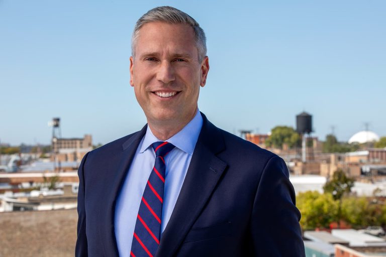 Half body portrait of Illinois Treasurer smiling against a backdrop of Chicago as seen from a rooftop