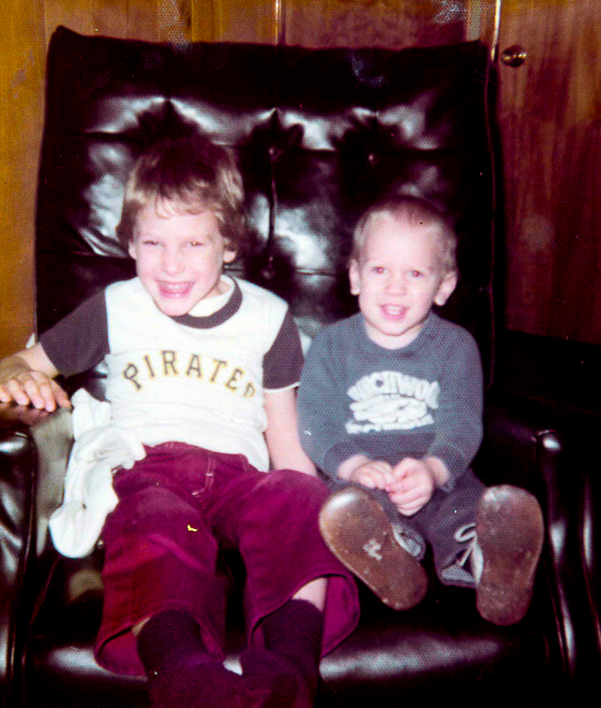 two boys sitting on a recliner smiling at the camera