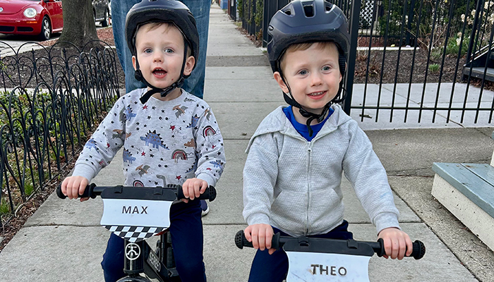 Twin toddler boys riding small bikes on a sidewalk